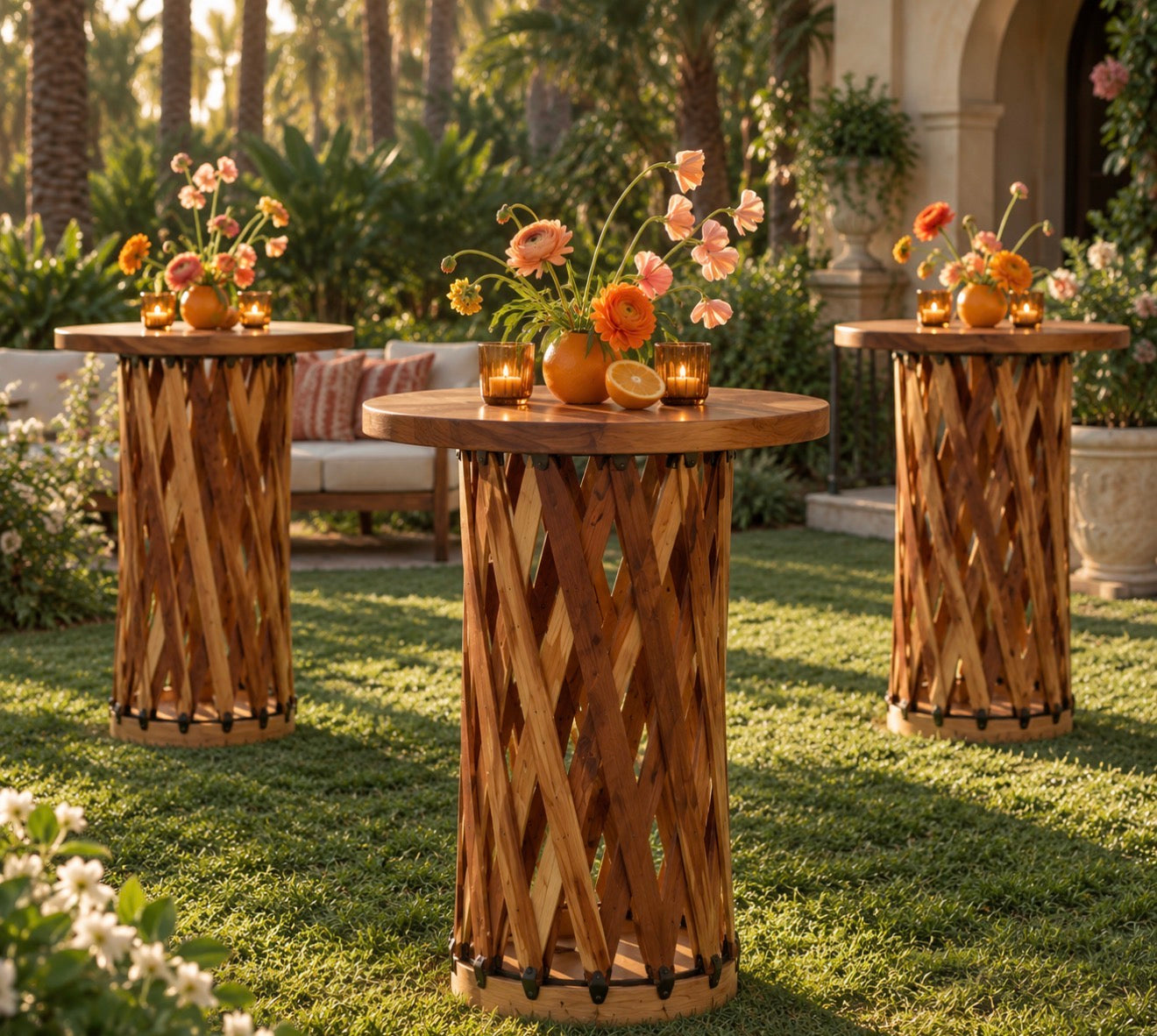 Three handcrafted woven wood cocktail tables with leather tops styled with orange floral arrangements and candles at an outdoor Florida garden wedding.